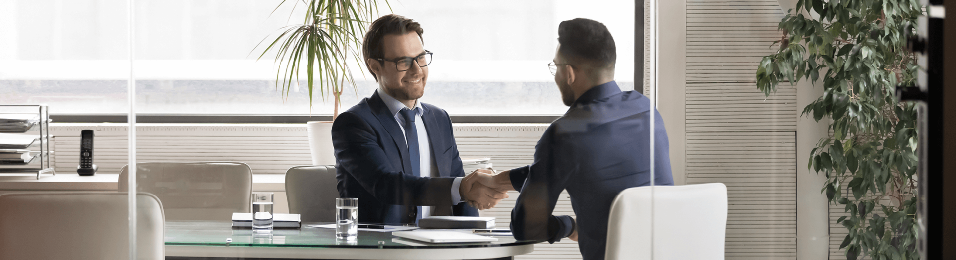 Two business people shaking hands in office setting behind a desk