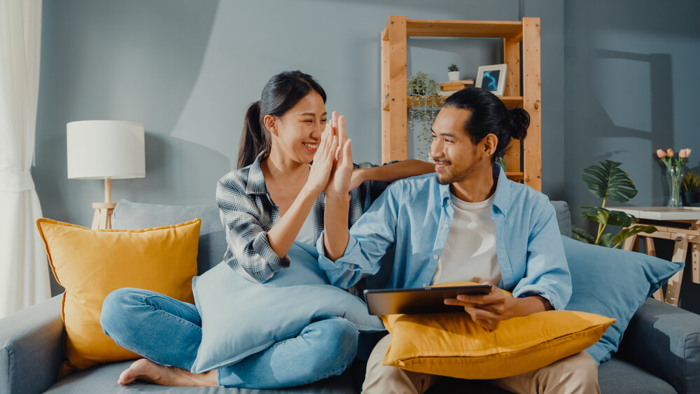 Young couple high-fiving on couch after applying for a home equity line of credit online