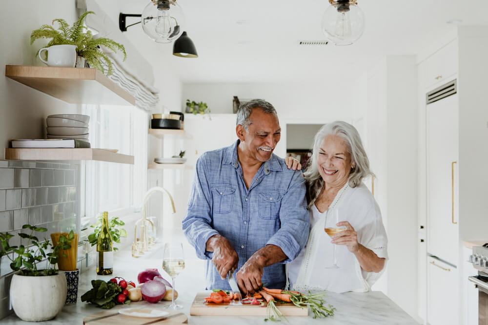 Elderly couple in kitchen slicing vegetables on cutting board