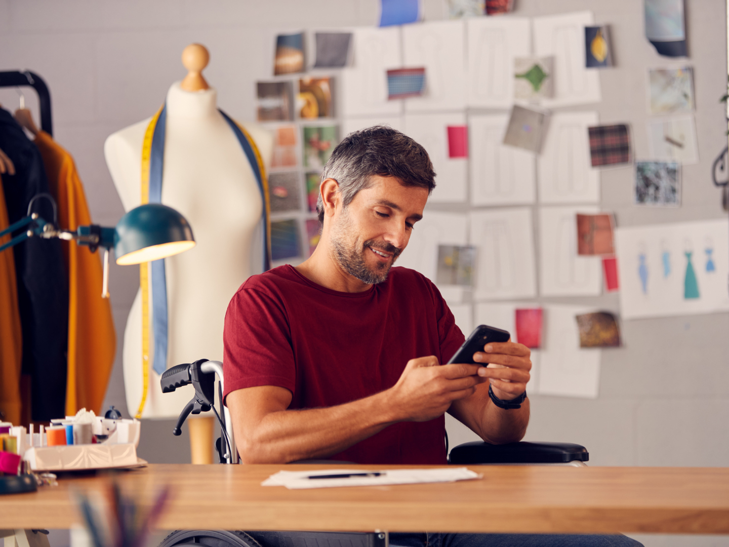 a designer sits in his wheelchair in his studio reviewing mobile banking options on his phone after learning more about business checking for entrepreneurs from quaint oak bank