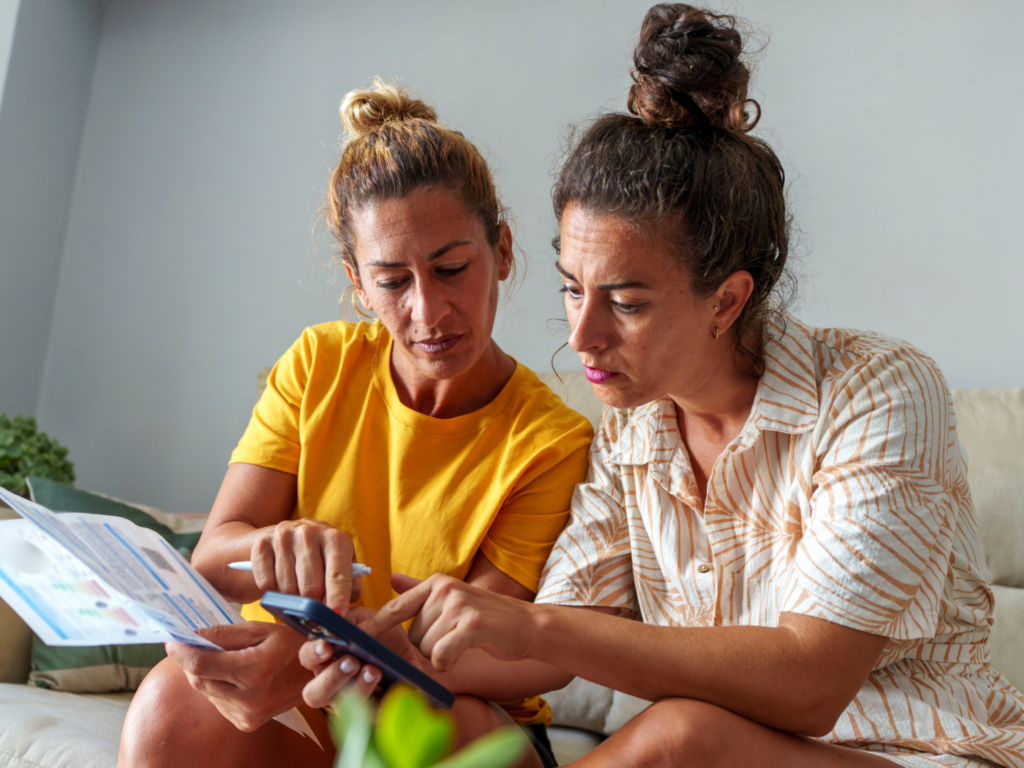 two women sitting together on a couch in their home reviewing their finances after learning more about the psychology of money management
